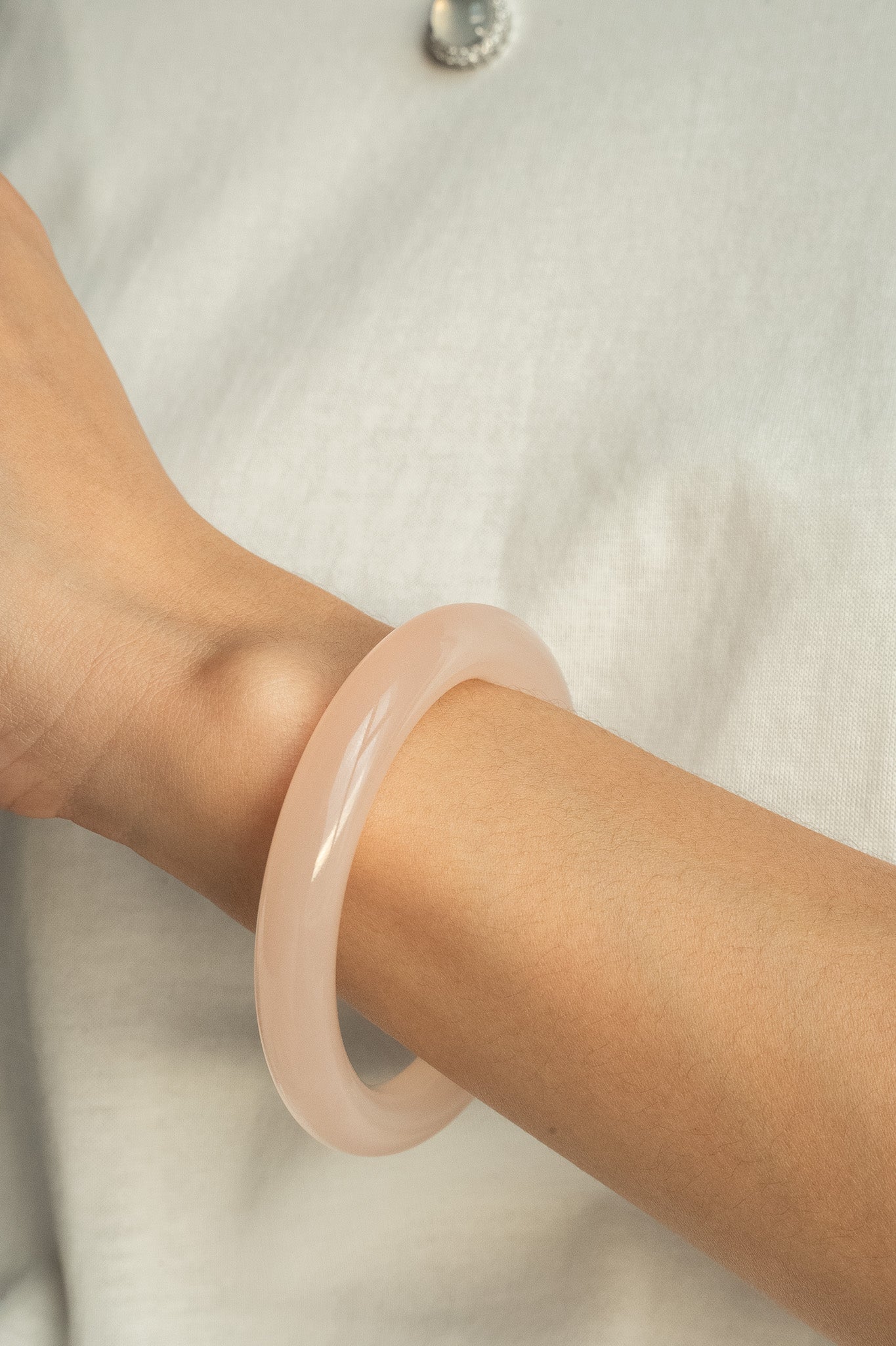 A soft, translucent blush-colored bangle bracelet worn on a wrist against a light neutral background.